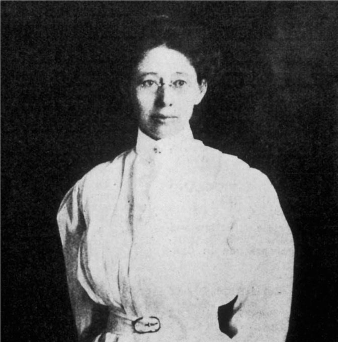 White woman with dark hear wearing a white dress and glasses, posing for a portrait