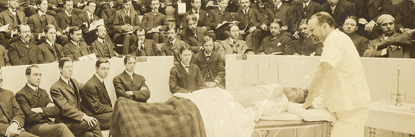 Murphy in an operating theater surrounded by an audience of men in suits