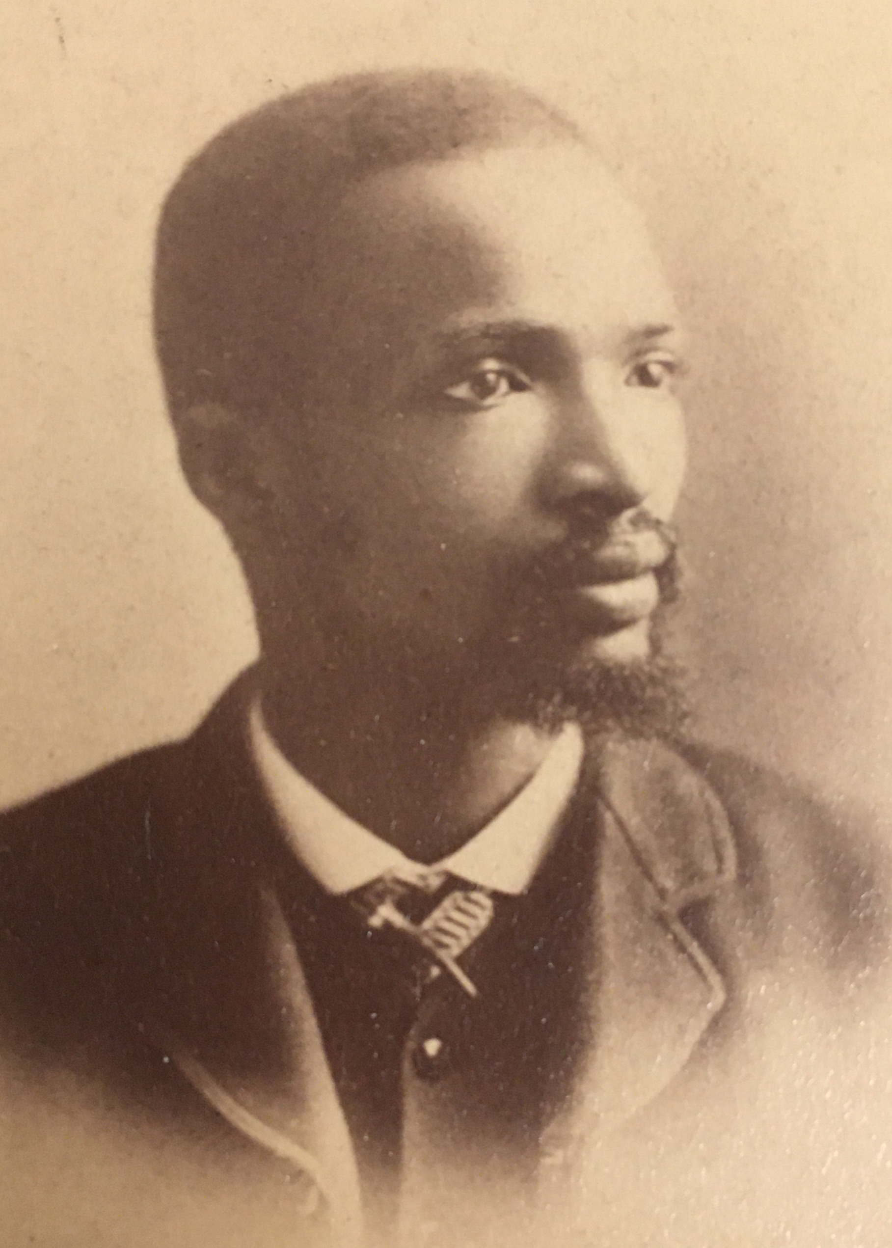 1887 portrait photograph of John Mavuma Nembula in sepia tones. Nembula has short hair, a goatee, and wears a suit and tie.
