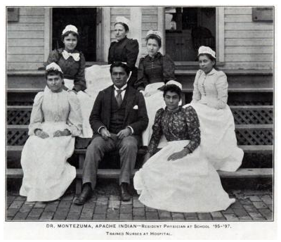 Carlos Montezuma and six women in nursing uniforms, all sitting on steps of the Carlisle Indian School clinic. Caption reads "Dr. Montezuma, Apache Indian-Resident Physician at School at Carlisle Indian School 1895-1897. Trained nurses at hospital."
