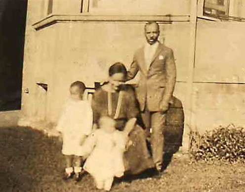 Dawson standing next to his seated wife and two children outside of a house
