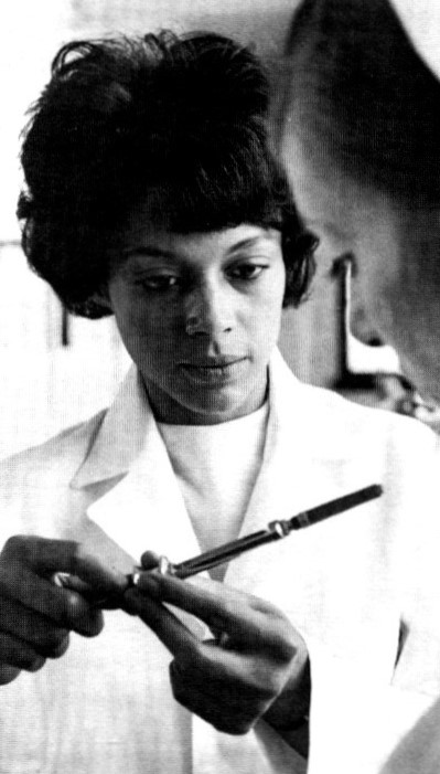 Young black woman in white lab coat showing an instrument to a student